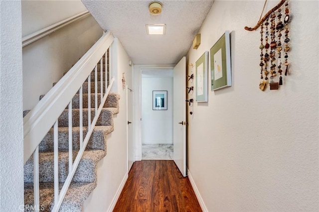 corridor featuring a textured ceiling, baseboards, stairs, and dark wood finished floors