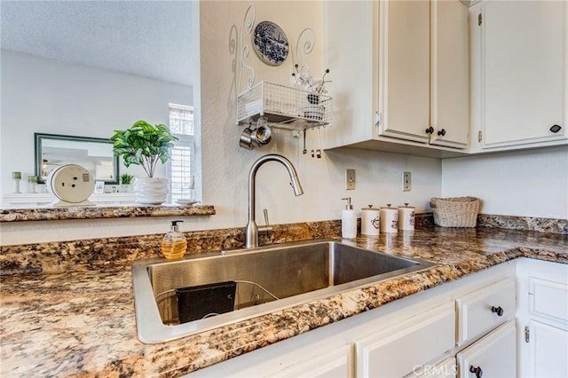 interior details with white cabinets, dark stone countertops, a sink, and a textured ceiling