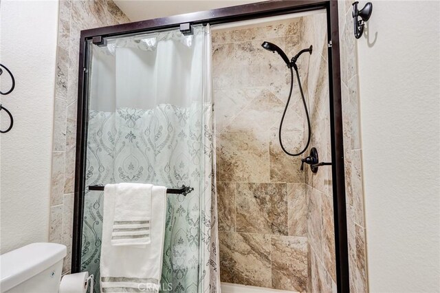 full bath featuring a shower stall, toilet, and a textured wall