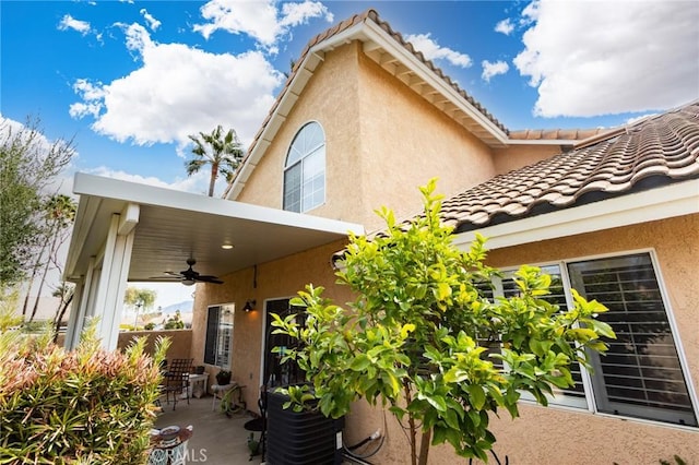 view of side of home with a ceiling fan, stucco siding, a tiled roof, and a patio