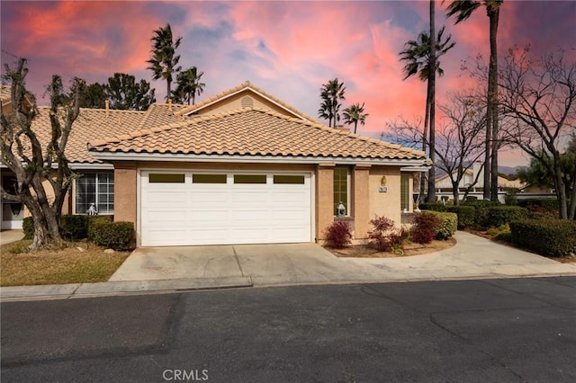 mediterranean / spanish home featuring a tile roof, concrete driveway, a garage, and stucco siding