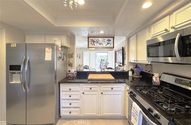 kitchen featuring appliances with stainless steel finishes, a tray ceiling, dark stone counters, crown molding, and white cabinets