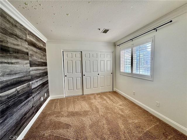 unfurnished bedroom with a textured ceiling, crown molding, wood walls, and carpet flooring