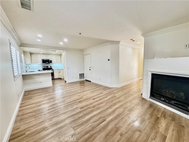 unfurnished living room with crown molding, sink, and light hardwood / wood-style flooring