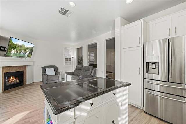 kitchen with white cabinetry, stainless steel refrigerator with ice dispenser, light hardwood / wood-style floors, and a tile fireplace