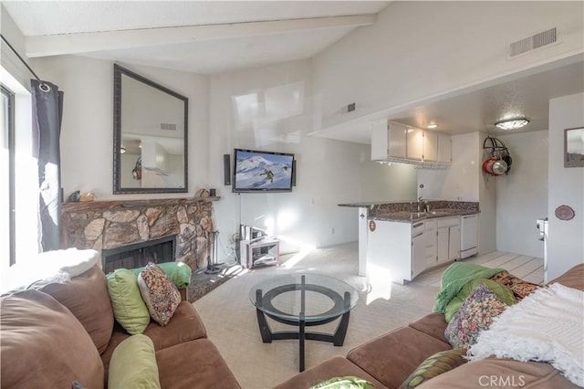 living room with sink, a stone fireplace, light colored carpet, and vaulted ceiling with beams