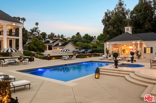 pool at dusk with an outbuilding, a patio area, and an in ground hot tub