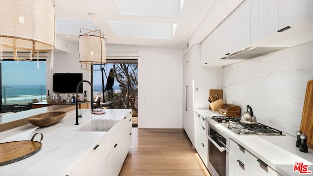 kitchen featuring a skylight, white cabinetry, appliances with stainless steel finishes, backsplash, and pendant lighting