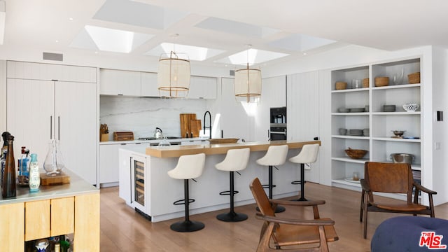 kitchen with white cabinets, decorative light fixtures, a skylight, a kitchen breakfast bar, and a center island with sink