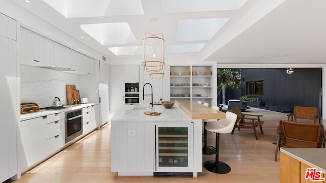 kitchen featuring white cabinetry, a kitchen island with sink, beverage cooler, and decorative light fixtures