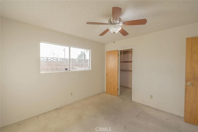 unfurnished bedroom with ceiling fan, a spacious closet, a textured ceiling, light carpet, and a closet