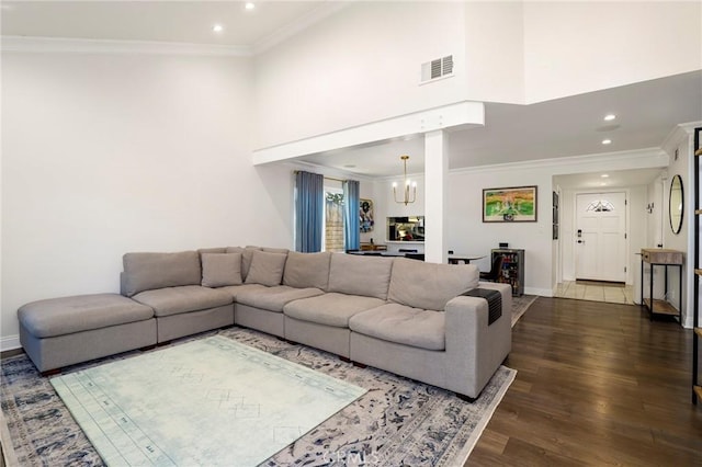 living room featuring dark wood-type flooring, crown molding, a high ceiling, and a notable chandelier