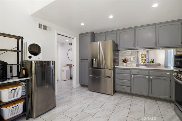 kitchen featuring washer / dryer, stainless steel appliances, gray cabinetry, and tasteful backsplash