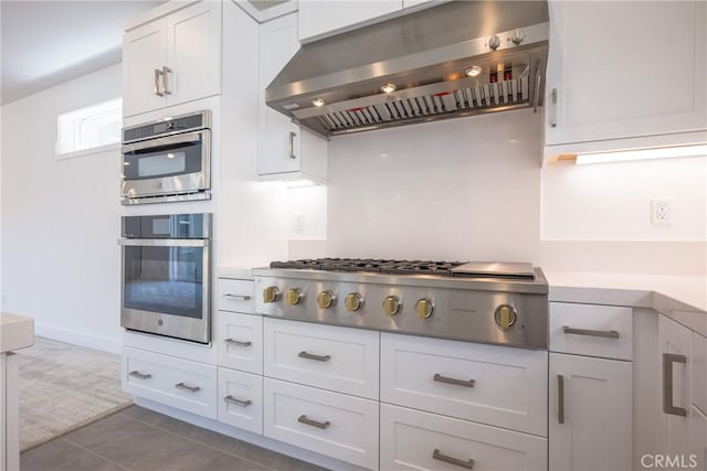 kitchen with dark tile patterned floors, white cabinetry, appliances with stainless steel finishes, and extractor fan