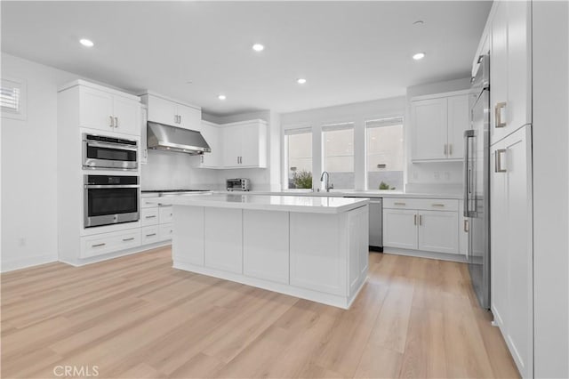 kitchen featuring stainless steel appliances, light hardwood / wood-style floors, white cabinets, and a kitchen island