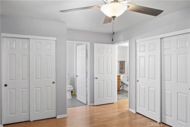 unfurnished bedroom featuring ceiling fan, ensuite bath, light wood-type flooring, and two closets