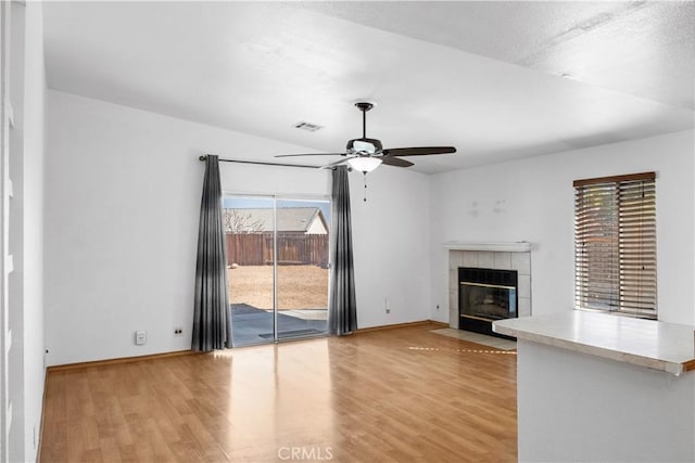 unfurnished living room featuring hardwood / wood-style flooring, ceiling fan, and a tiled fireplace