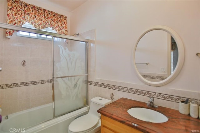 full bathroom with toilet, enclosed tub / shower combo, tile walls, and vanity