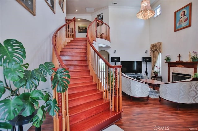 stairway featuring a notable chandelier, a towering ceiling, ornamental molding, and hardwood / wood-style floors