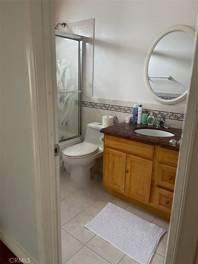 full bathroom featuring tile patterned flooring, vanity, tile walls, toilet, and combined bath / shower with glass door