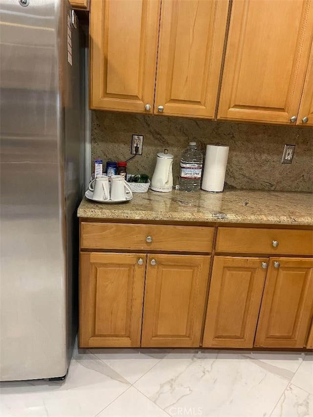 kitchen featuring tasteful backsplash, stainless steel fridge, and light stone counters