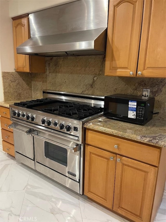 kitchen with light stone counters, range with two ovens, wall chimney range hood, and tasteful backsplash