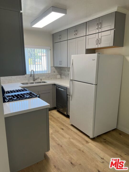 kitchen with dishwasher, white fridge, light hardwood / wood-style floors, sink, and gray cabinetry