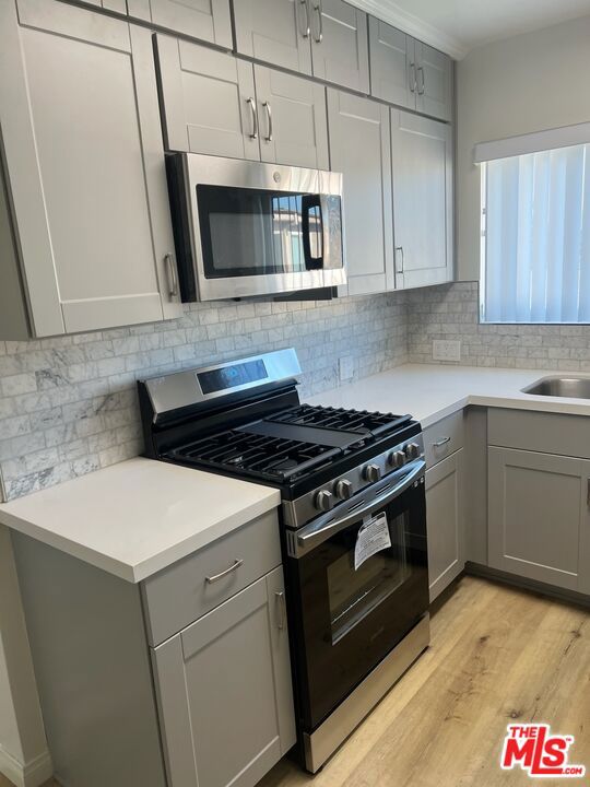 kitchen featuring light hardwood / wood-style floors, gray cabinets, appliances with stainless steel finishes, backsplash, and sink