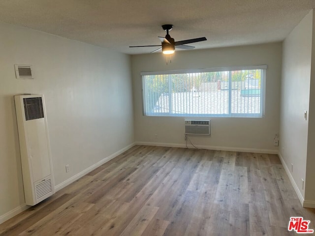 unfurnished room featuring a wall unit AC, ceiling fan, a textured ceiling, and light hardwood / wood-style flooring