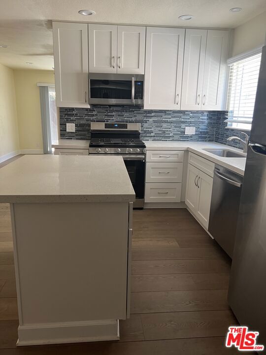 kitchen featuring white cabinetry, appliances with stainless steel finishes, dark hardwood / wood-style floors, a kitchen island, and sink