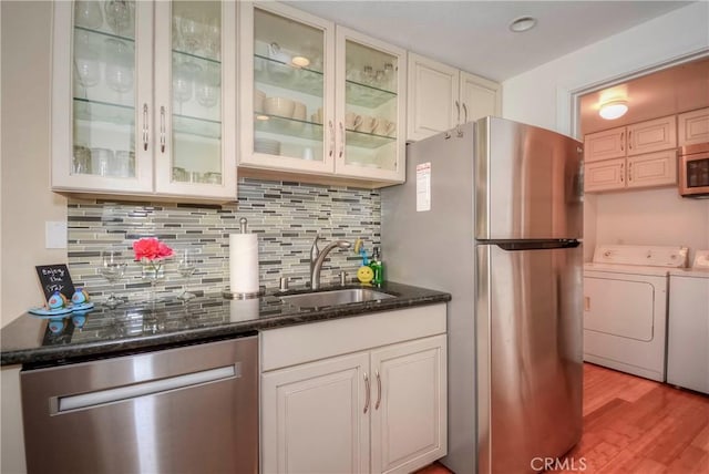 kitchen featuring washer and dryer, appliances with stainless steel finishes, dark stone countertops, decorative backsplash, and sink