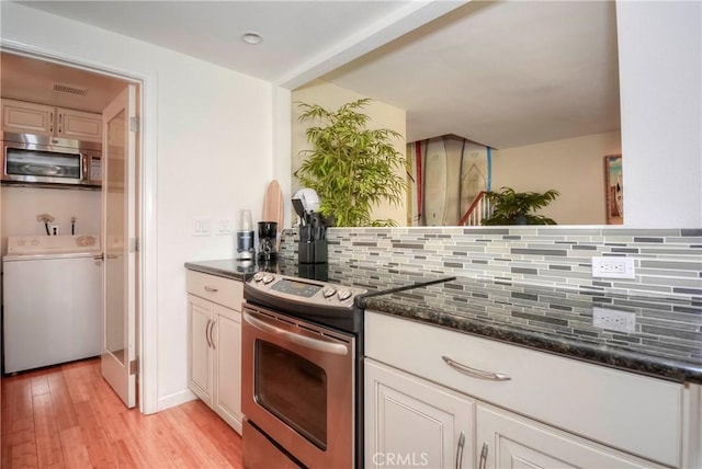 kitchen featuring washing machine and clothes dryer, stainless steel appliances, tasteful backsplash, dark stone countertops, and light hardwood / wood-style flooring