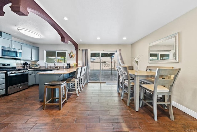 kitchen featuring a kitchen breakfast bar, gray cabinets, stainless steel appliances, and tasteful backsplash