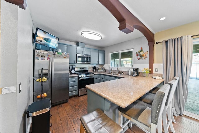 kitchen with a kitchen breakfast bar, kitchen peninsula, appliances with stainless steel finishes, and sink