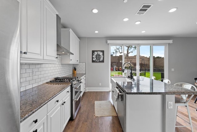 kitchen with an island with sink, sink, dark stone countertops, white cabinets, and stainless steel appliances