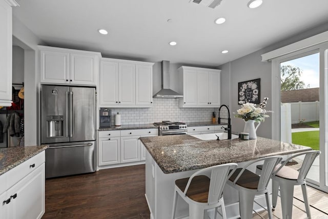 kitchen with wall chimney exhaust hood, sink, a center island with sink, premium appliances, and white cabinets