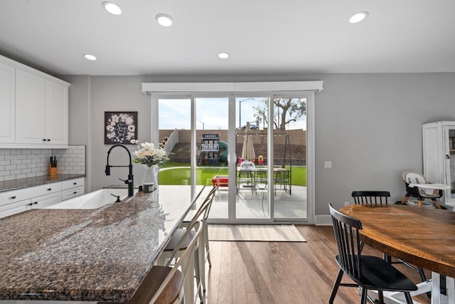 kitchen featuring light hardwood / wood-style flooring, a center island with sink, dark stone countertops, white cabinets, and backsplash