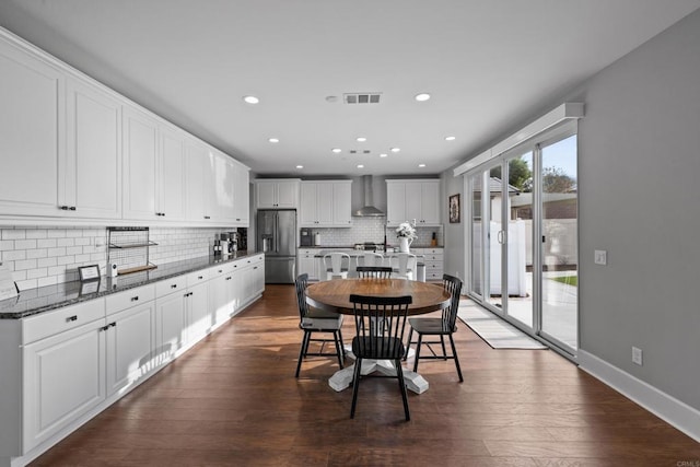 interior space with wall chimney range hood, white cabinetry, high end refrigerator, and dark stone counters