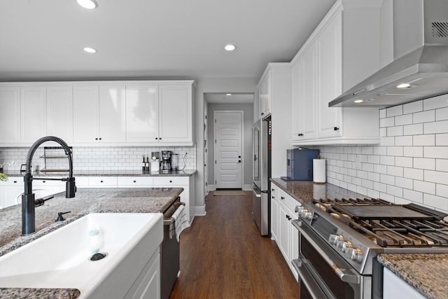 kitchen featuring wall chimney range hood, premium appliances, dark wood-style floors, white cabinetry, and a sink