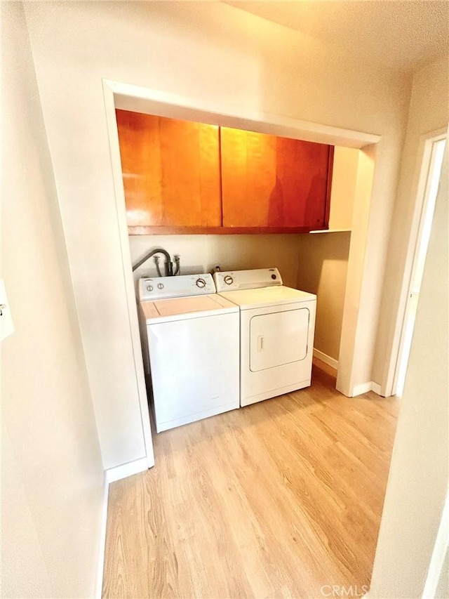 washroom with light hardwood / wood-style floors, cabinets, and washing machine and clothes dryer