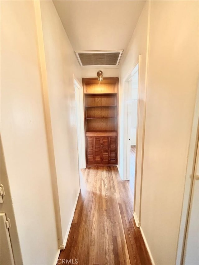 hall with built in shelves and wood-type flooring