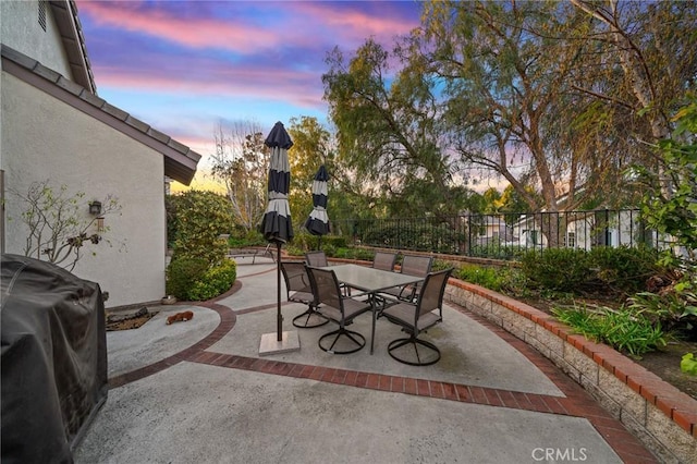 patio terrace at dusk featuring grilling area, outdoor dining space, and fence