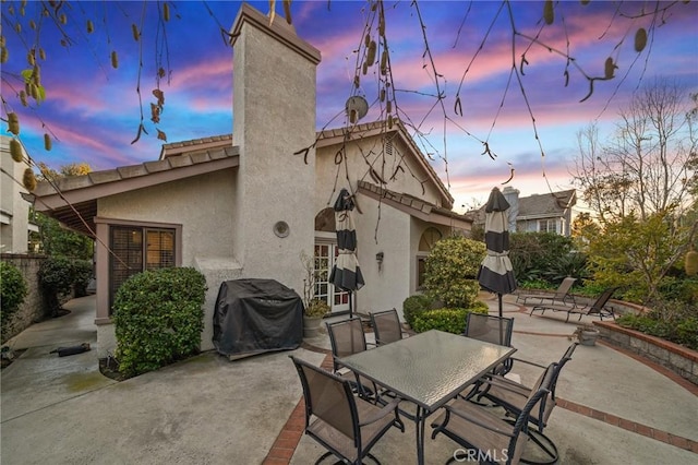 back of house at dusk featuring a chimney, a patio area, and stucco siding