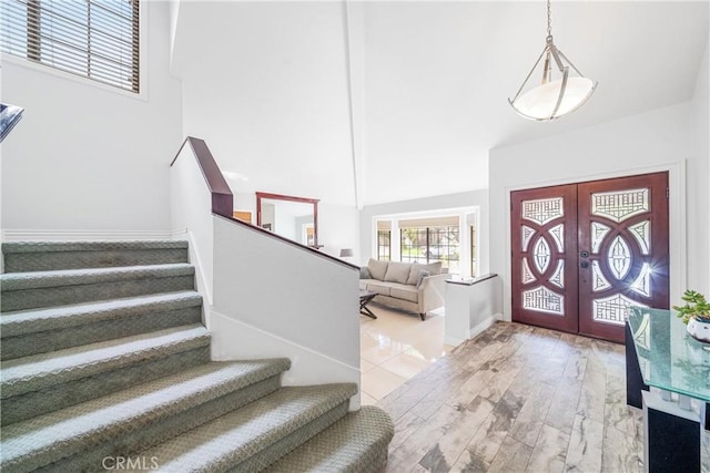 foyer entrance featuring french doors, stairway, a towering ceiling, wood finished floors, and baseboards