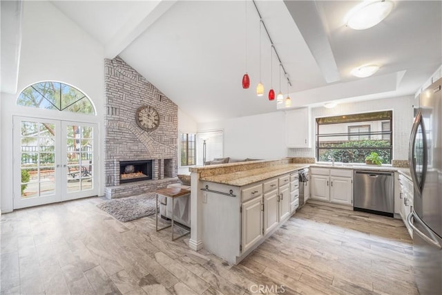 kitchen with light wood-style floors, a peninsula, light stone countertops, stainless steel appliances, and a brick fireplace