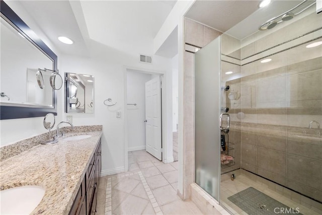 full bath with double vanity, visible vents, a sink, a shower stall, and baseboards