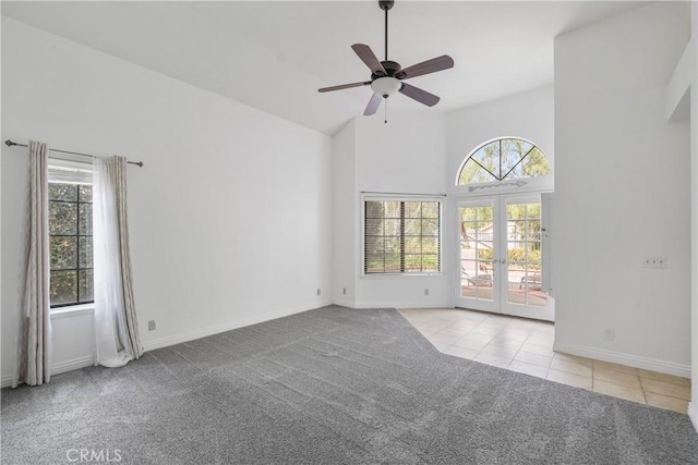 carpeted empty room featuring baseboards, a ceiling fan, tile patterned flooring, french doors, and high vaulted ceiling