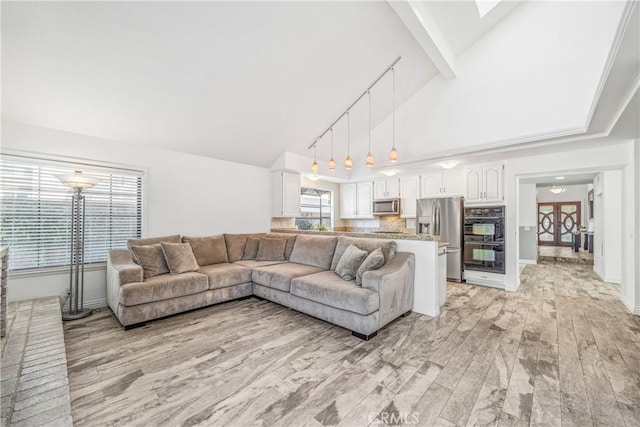 living area featuring track lighting, light wood-style flooring, high vaulted ceiling, and baseboards