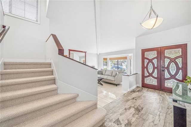 entrance foyer featuring baseboards, stairs, french doors, wood finished floors, and high vaulted ceiling