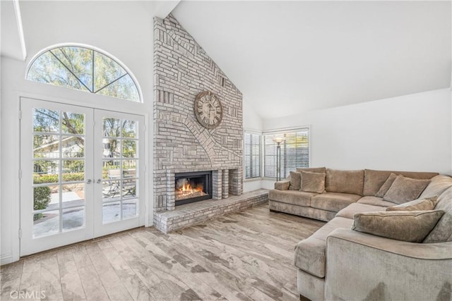 living room with plenty of natural light, a brick fireplace, high vaulted ceiling, and wood finished floors